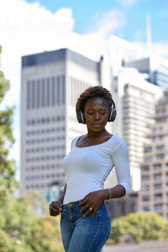 Young African woman listening to music wearing wireless headphones in city - Australian Stock Image