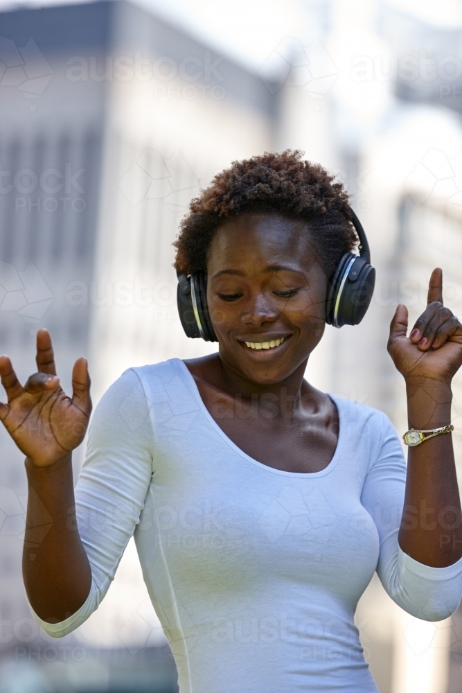 Young African woman listening to music wearing wireless headphones in city - Australian Stock Image