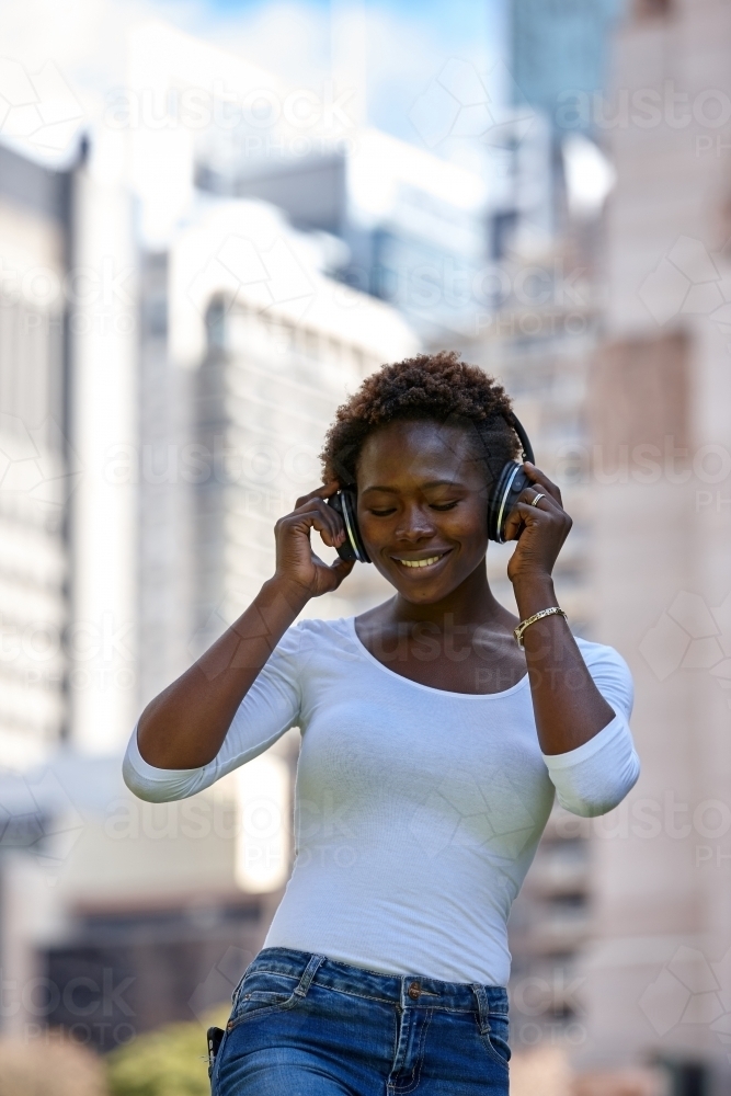 Young African woman listening to music wearing wireless headphones in city - Australian Stock Image