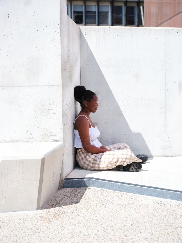 Young African woman sitting against a concrete wall - Australian Stock Image