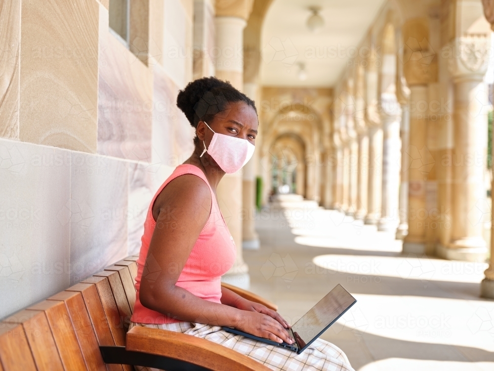 Young African woman wearing a mask at a university campus - Australian Stock Image