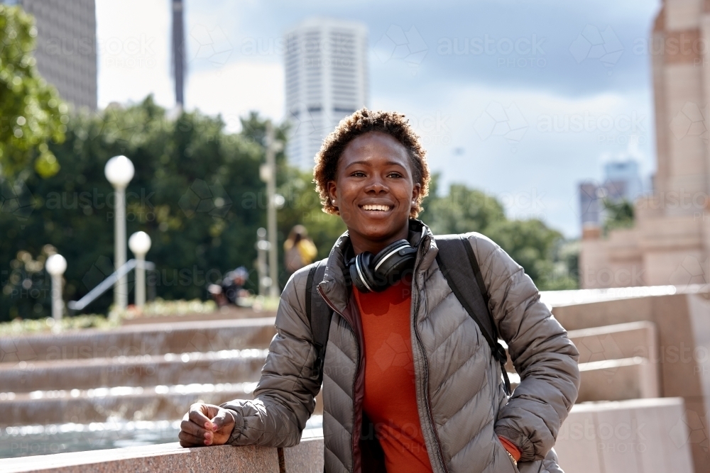 Young African woman wearing wireless headphones in city - Australian Stock Image