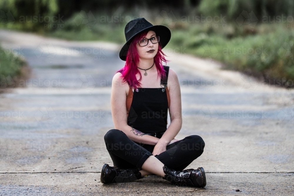 Young alternative woman sitting cross legged on road - Australian Stock Image