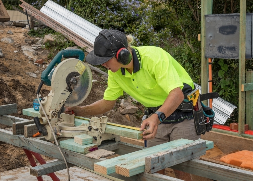 Young apprentice builder cutting timber with drop saw on residential construction site - Australian Stock Image