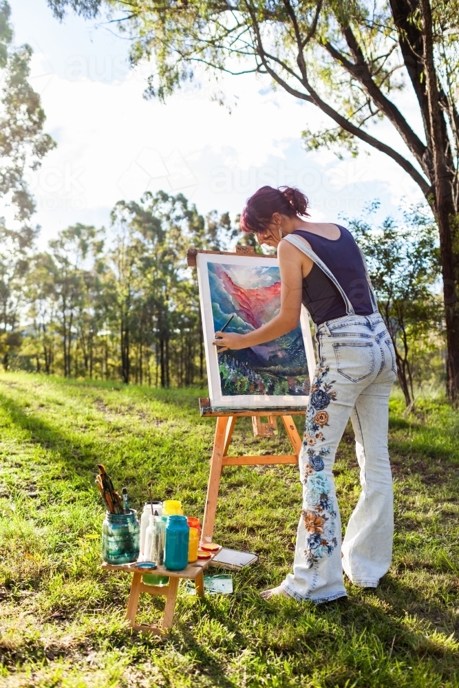 Image of Young artist in overalls painting art outside in nature
