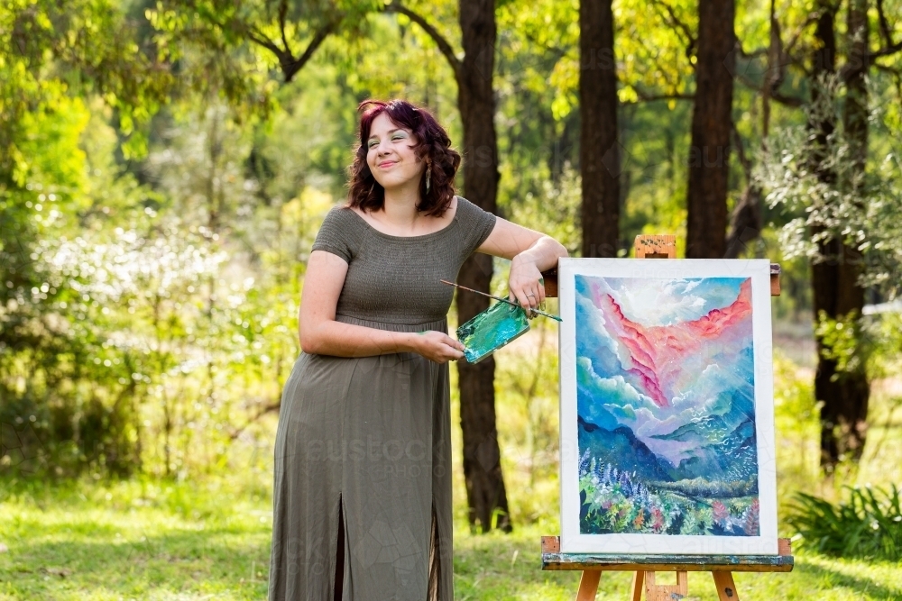 Young artist standing beside acrylic painting outside looking up - Australian Stock Image
