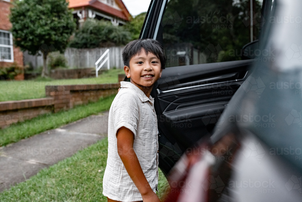 Young Asian boy standing beside the car door - Australian Stock Image