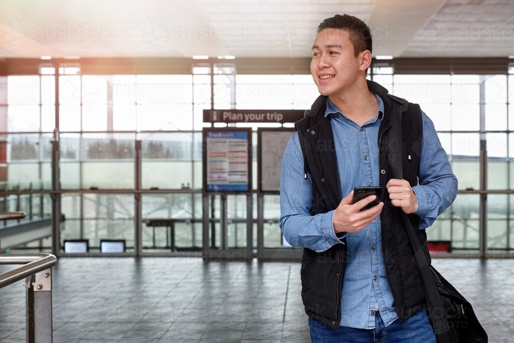 Young Asian commuter holding phone walking out from train station - Australian Stock Image