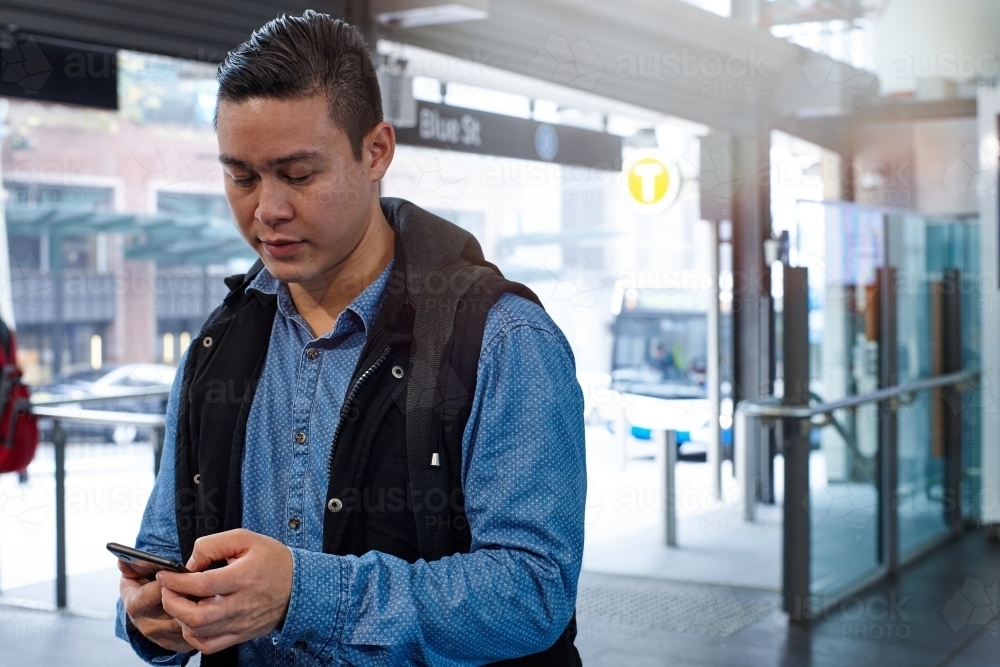 Young Asian commuter using mobile phone at train station entrance - Australian Stock Image