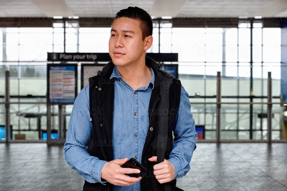 Young Asian commuter waiting at train station entrance - Australian Stock Image