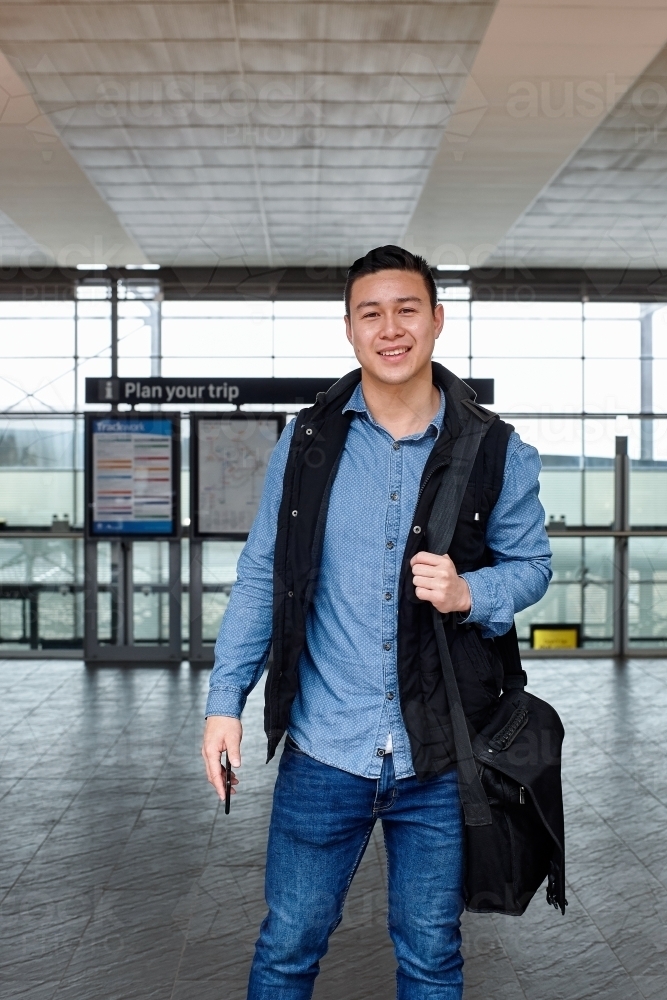 Young Asian commuter waiting at train station entrance - Australian Stock Image