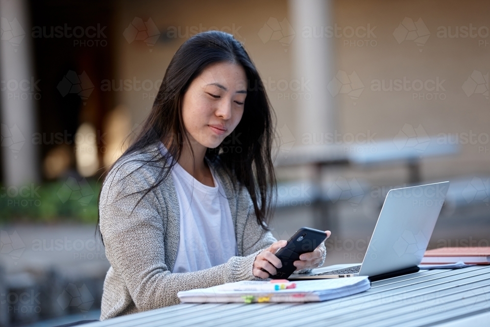 Young Asian female university student studying on laptop outdoors - Australian Stock Image