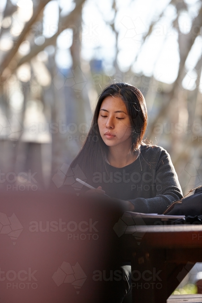 Young Asian female university student studying outdoors - Australian Stock Image