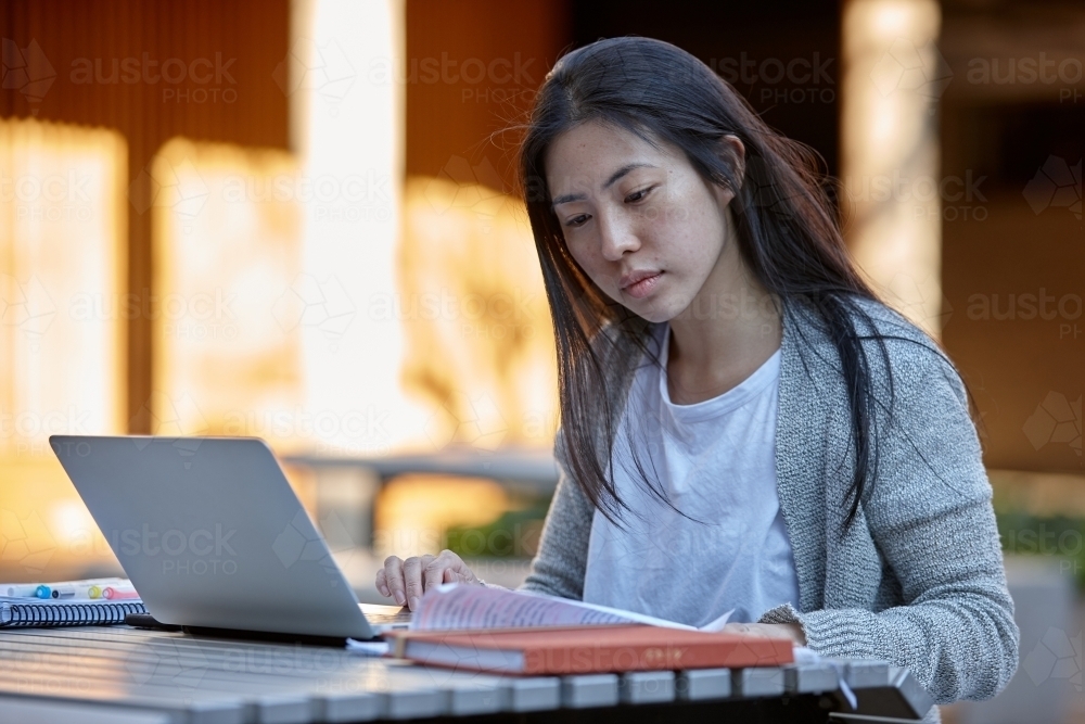 Young Asian female university student studying outside with a laptop - Australian Stock Image