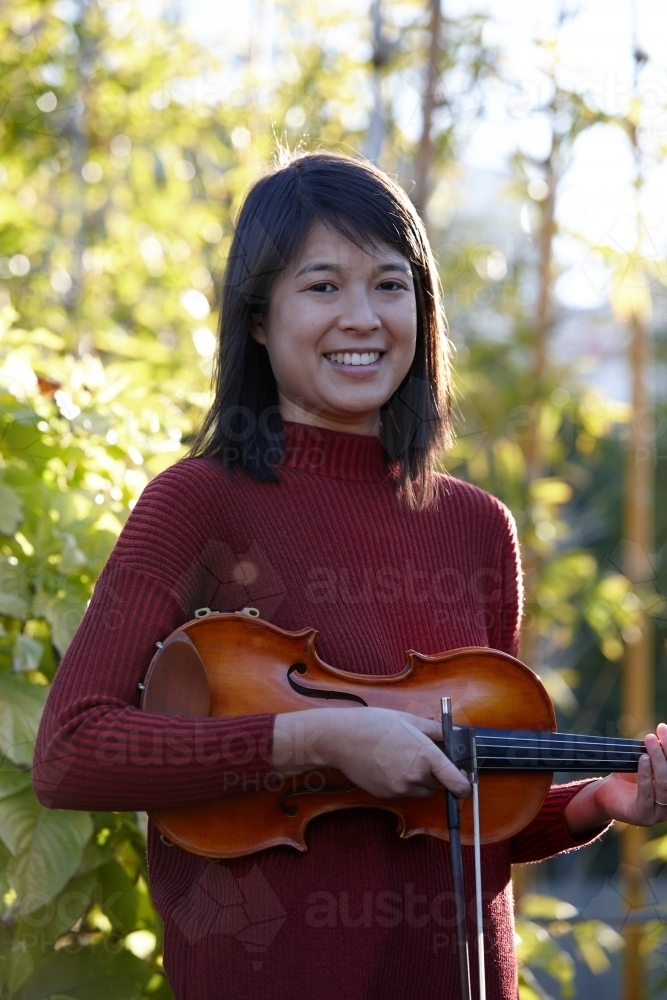 Young Asian female violin player practising outdoors - Australian Stock Image