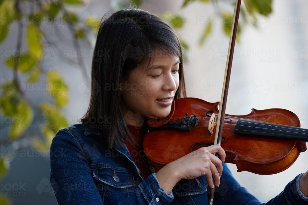 Young Asian female violin player practising outdoors - Australian Stock Image
