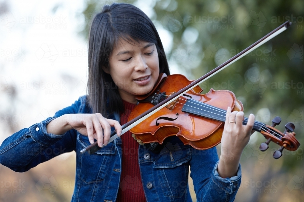 Young Asian female violin player practising outdoors - Australian Stock Image