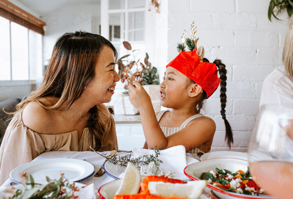 Young Asian girl holding cracker joke piece of paper at dinner table during christmas celebration - Australian Stock Image
