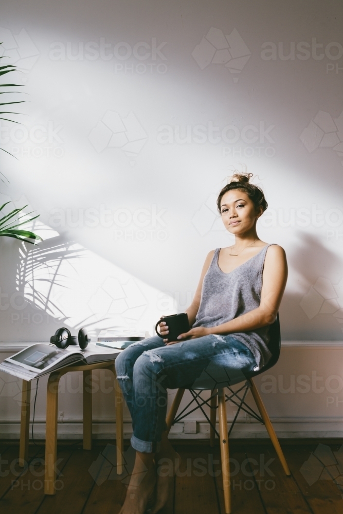 Young asian girl looking contently into camera at home in her apartment - Australian Stock Image