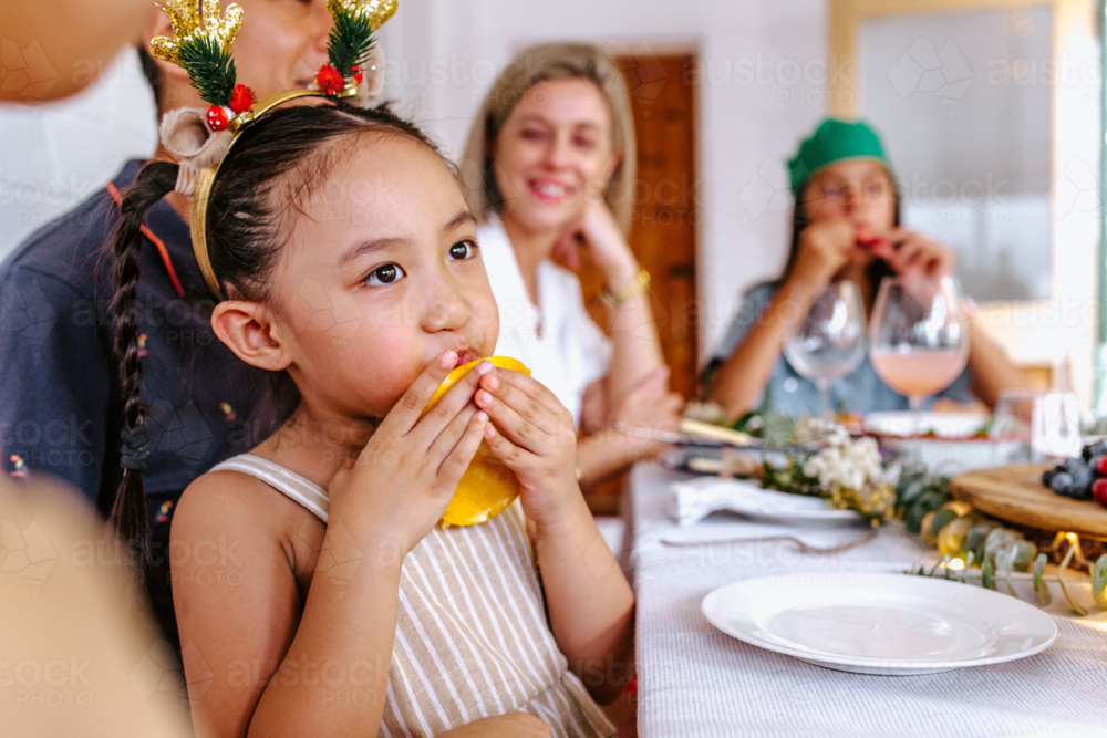 Young Asian girl with Christmas reindeer antler headband enjoying ripe mango - Australian Stock Image