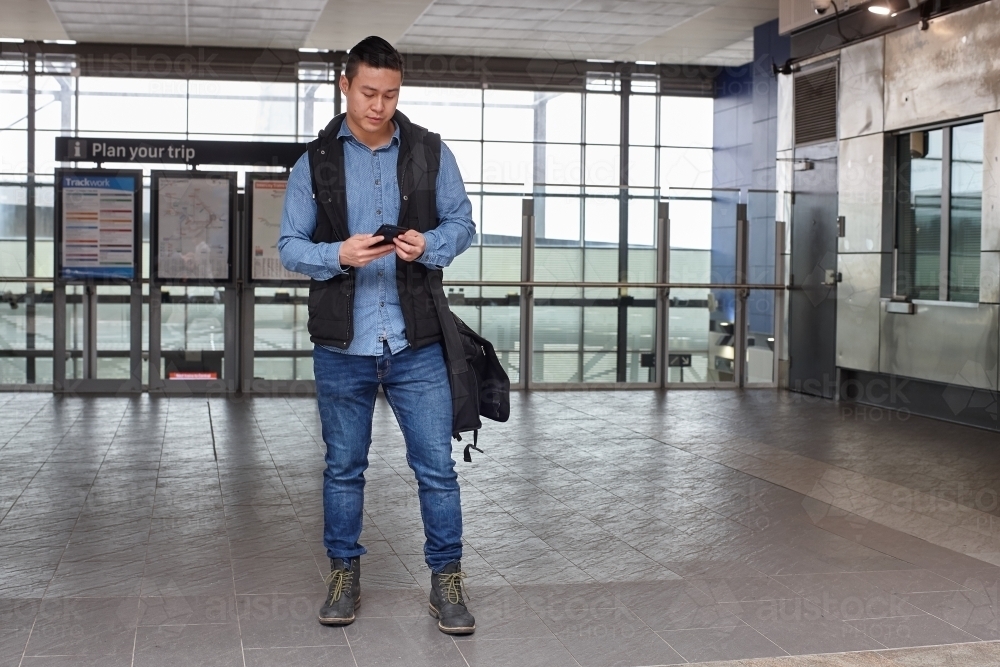 Young Asian man checking mobile device at train station - Australian Stock Image
