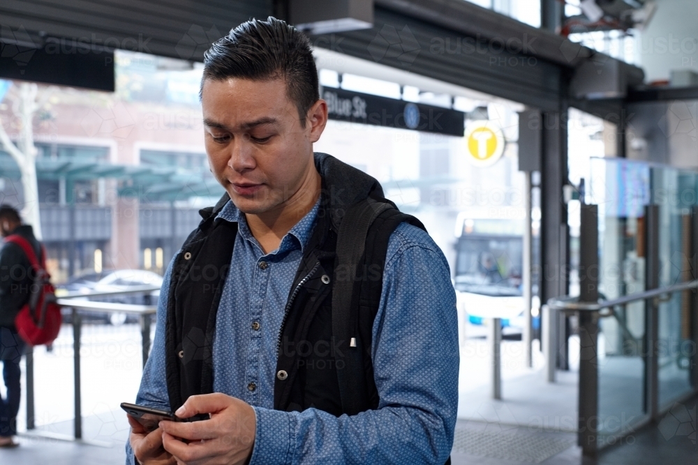 Young Asian man checking mobile device at train station - Australian Stock Image