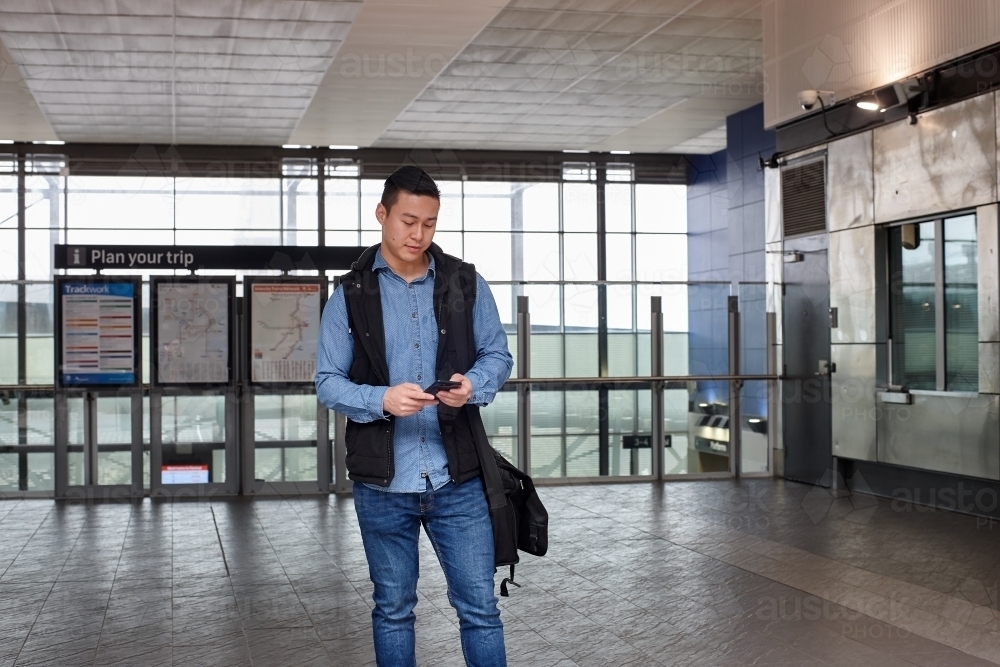 Young Asian man checking mobile device at train station - Australian Stock Image