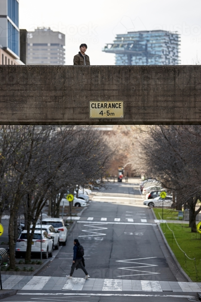 Young Asian man standing on bridge with city in background - Australian Stock Image