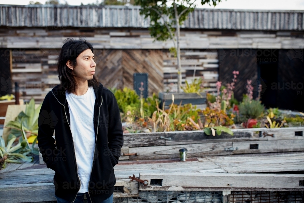 Young Asian man standing outside in warehouse courtyard - Australian Stock Image