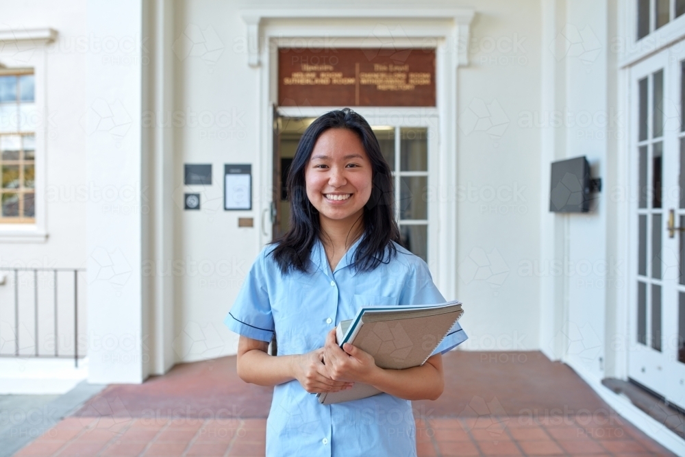 Young Asian student in front of school building holding books - Australian Stock Image