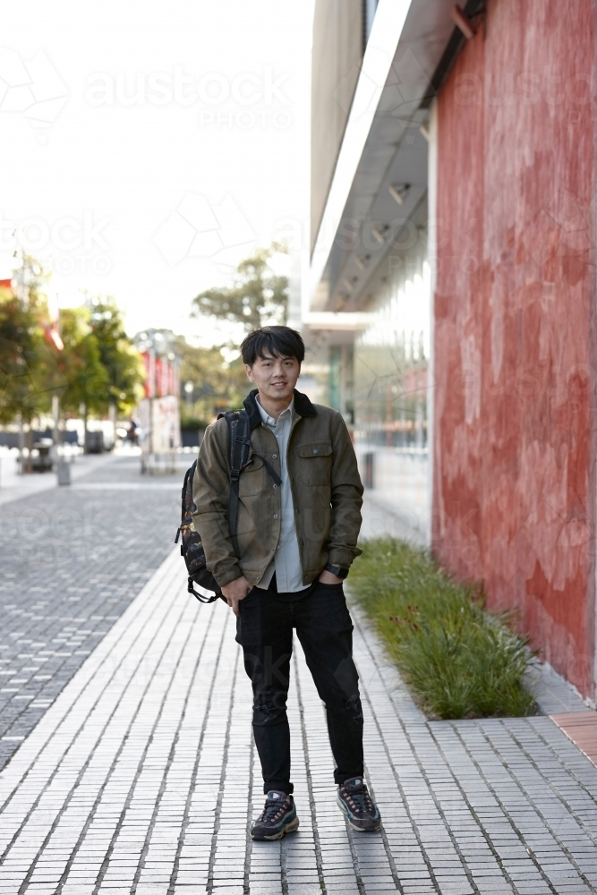 Young Asian student standing outside the university campus - Australian Stock Image