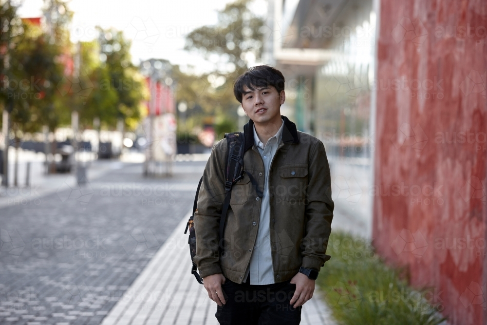 Young Asian student standing outside the university campus - Australian Stock Image