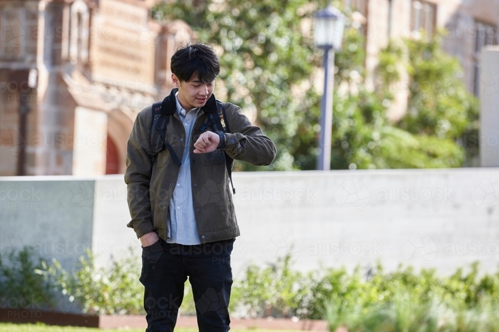 Young Asian university student standing on-campus checking smart watch - Australian Stock Image