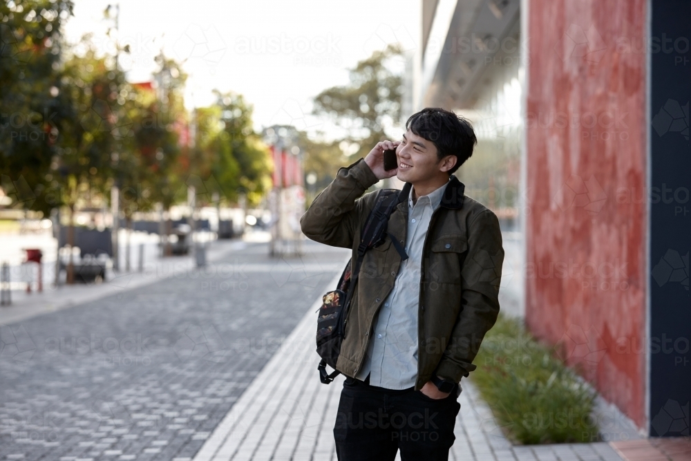 Young Asian university student walking and talking on his phone on-campus - Australian Stock Image