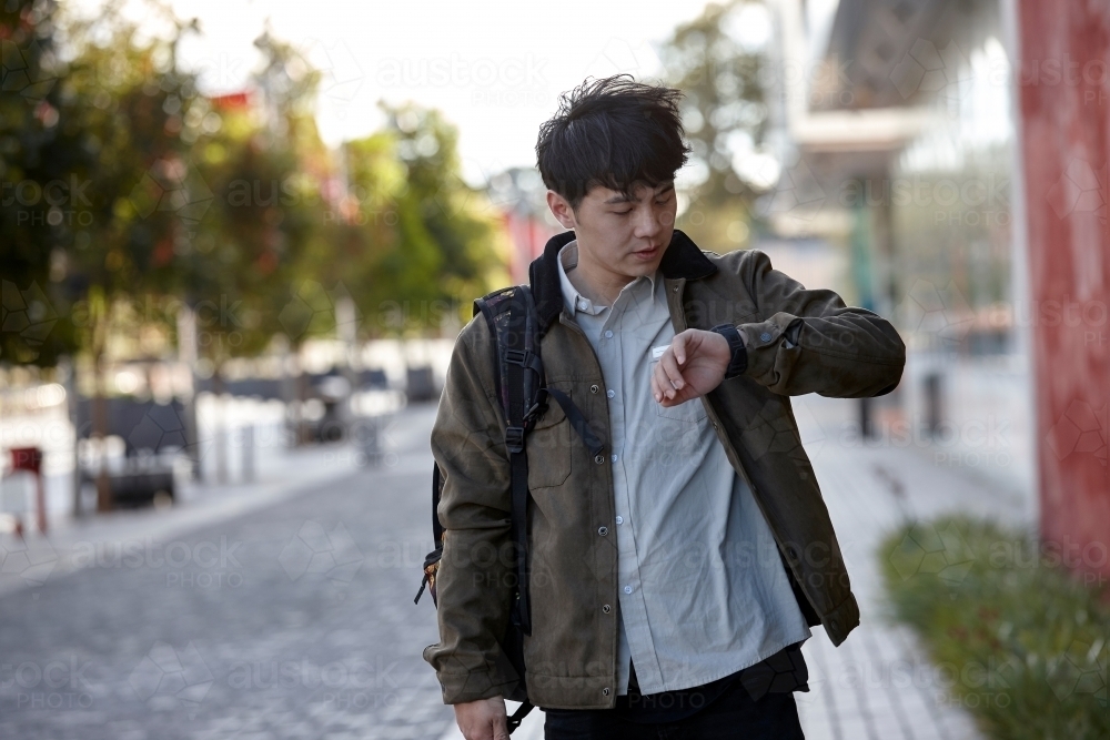 Young Asian university student walking on-campus checking smart watch - Australian Stock Image