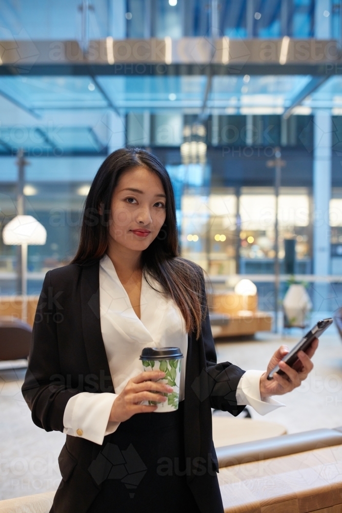 Young Asian woman in office building cafe using mobile phone - Australian Stock Image