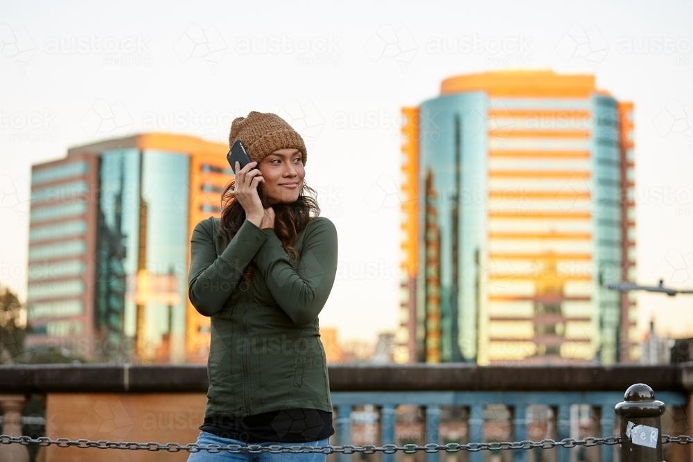 Young Asian woman talking on mobile phone in city on dusk - Australian Stock Image