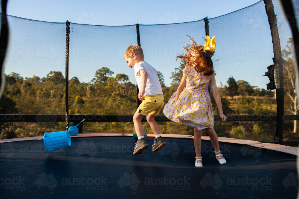 young aussie brother and sister jumping on trampoline in backyard together - Australian Stock Image