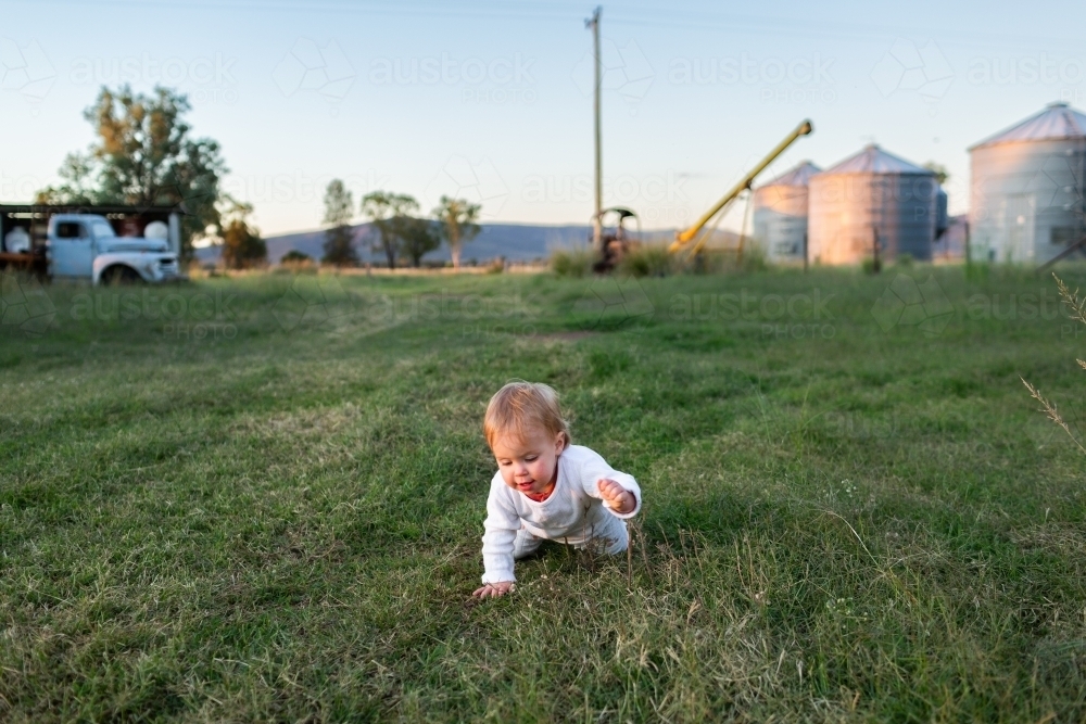 Young aussie country kid crawling through grass on farm on autumn evening - Australian Stock Image