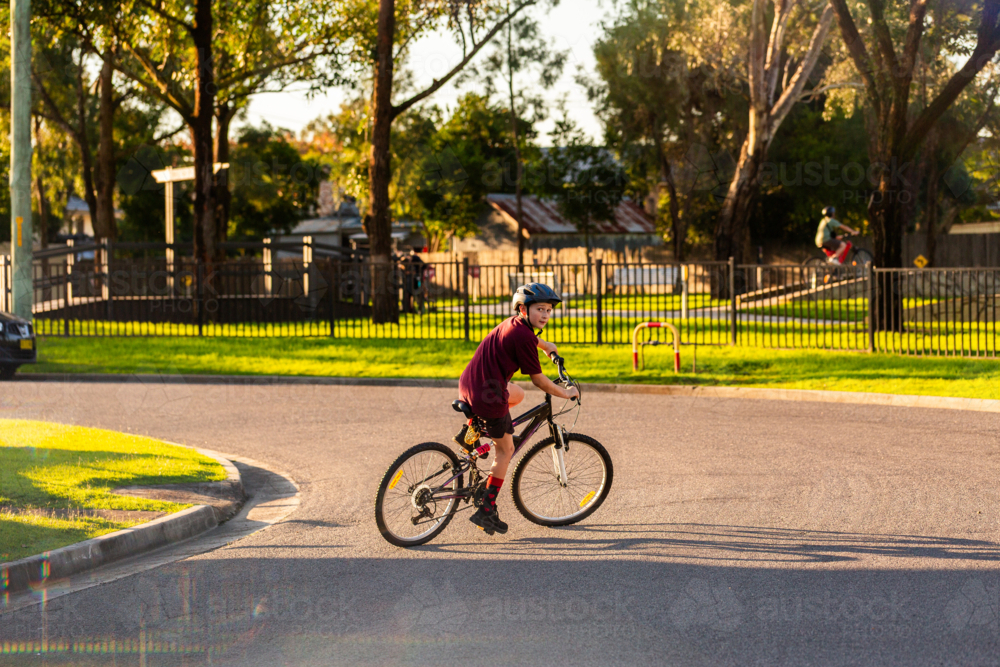 young Aussie kid on his bike riding on street in town wearing helmet - Australian Stock Image