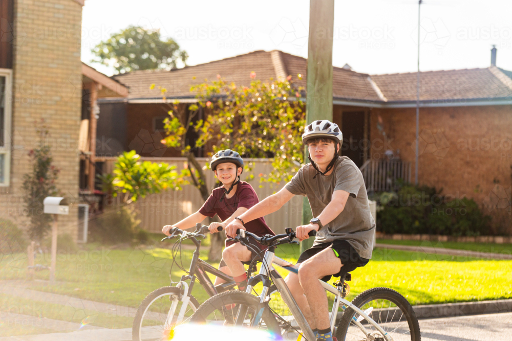 Young Aussie kids riding pushbikes cycling along on road in Australian country town - Australian Stock Image
