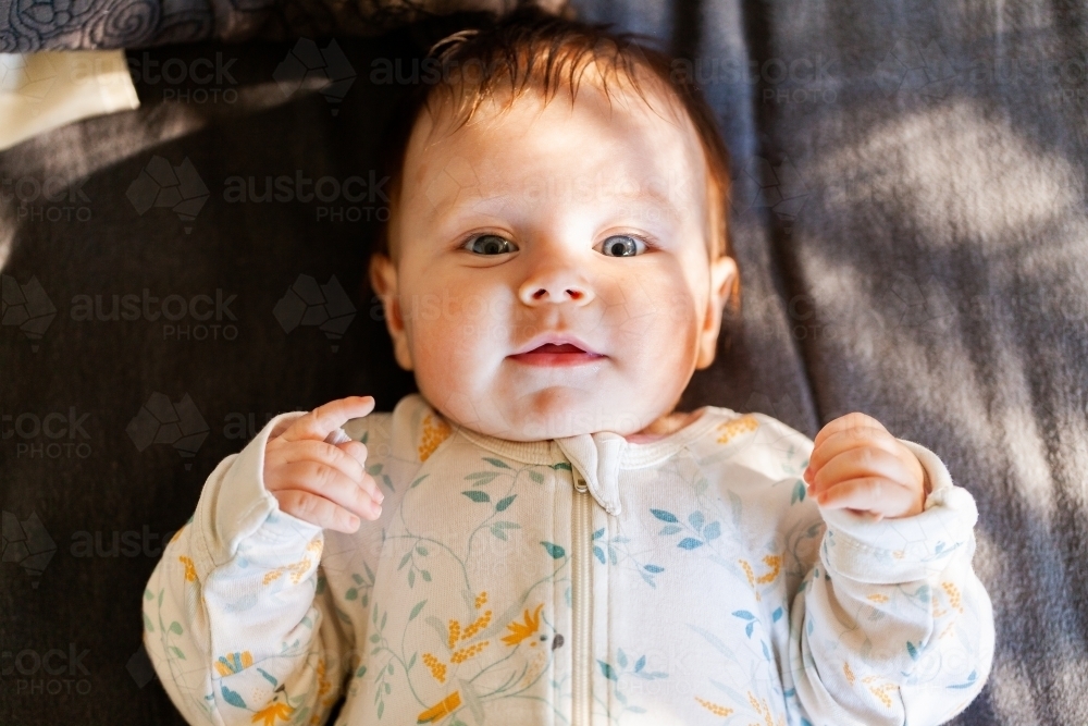 Young Australian baby lying on bed looking up with morning sunlight coming through window - Australian Stock Image