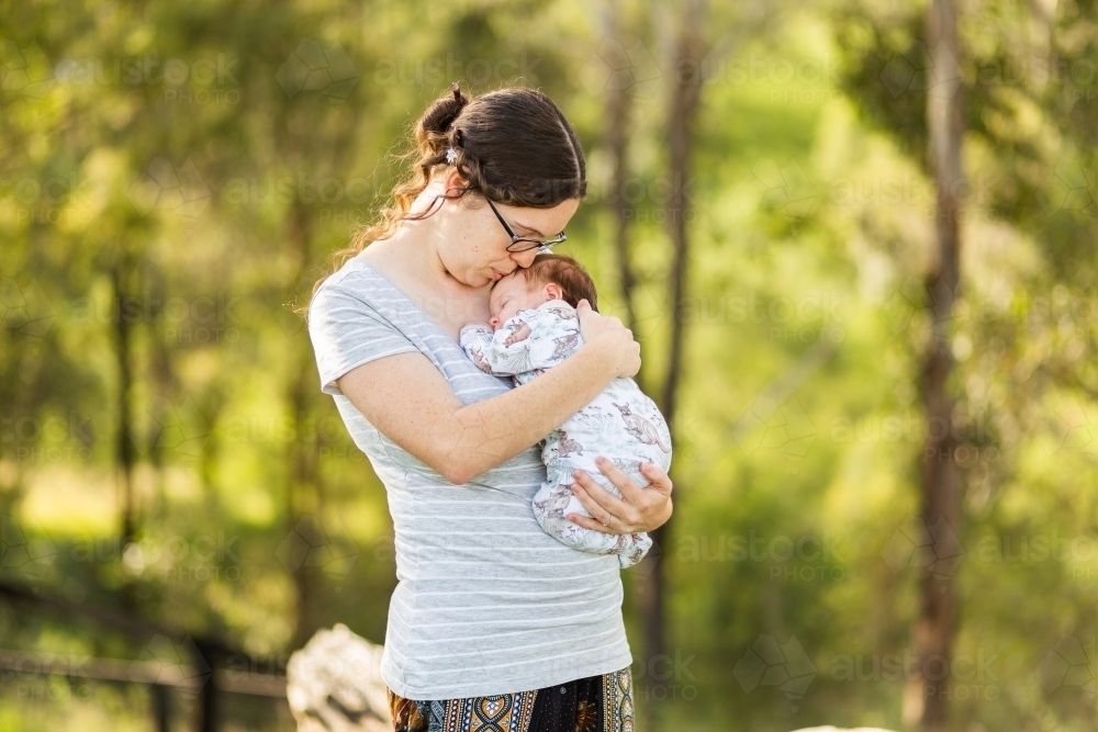 Young Australian mother standing outside cuddling a newborn baby - postpartum mental health - Australian Stock Image
