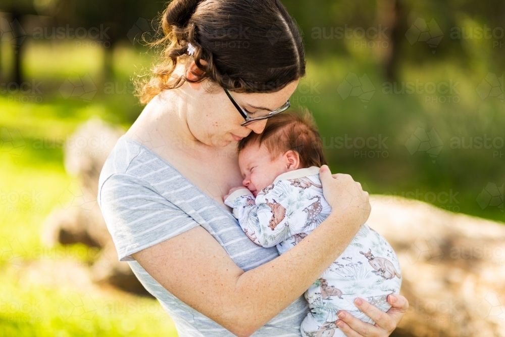 Young Australian mother standing outside cuddling a newborn baby - postpartum mental health - Australian Stock Image