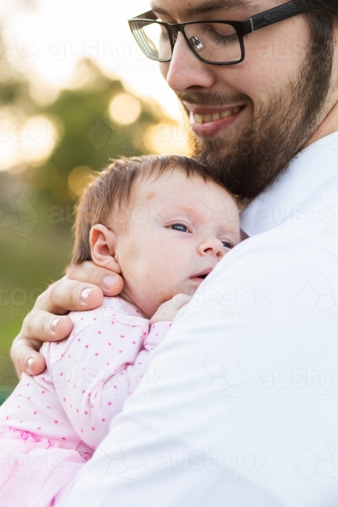 Young bearded dad smiling as he holds his newborn daughter close - Australian Stock Image