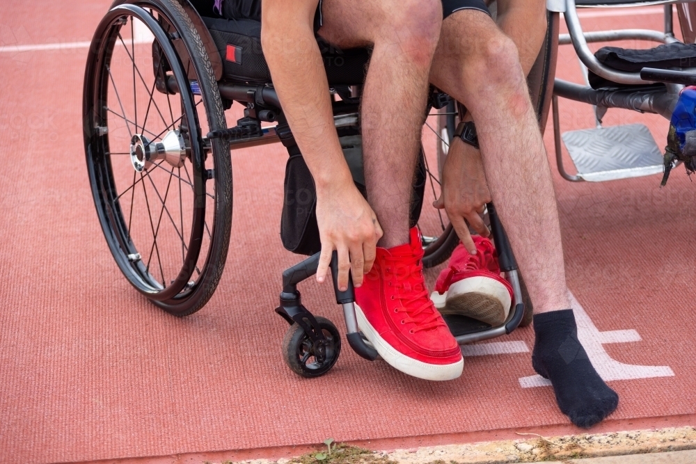 young bloke in wheelchair putting on red shoes - Australian Stock Image