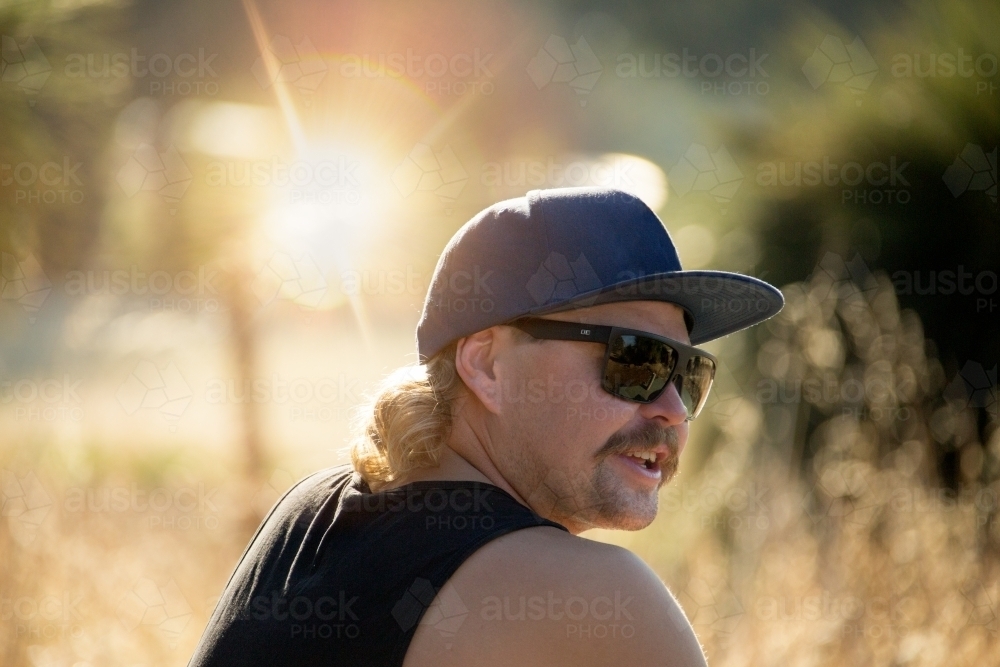Young bloke with moustache wearing sunnies, cap and singlet - Australian Stock Image
