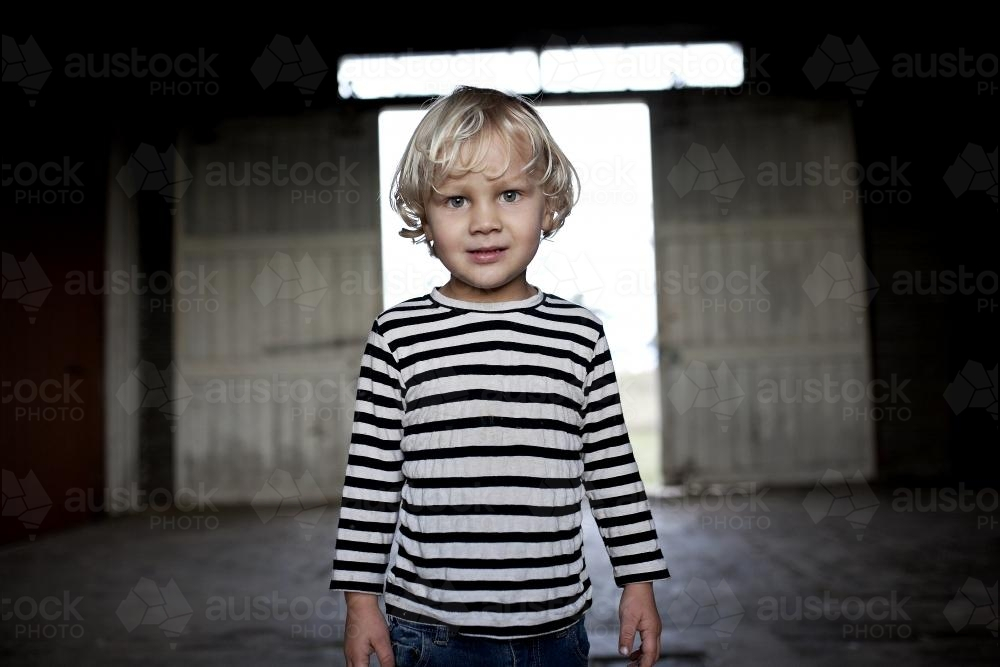 Young blond boy with background of dimly lit shed - Australian Stock Image