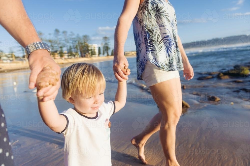 Young blonde boy holding his mum and dads hands at the beach - Australian Stock Image