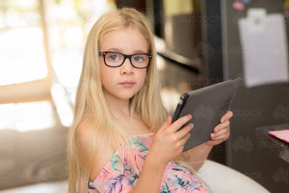 Young blonde girl looking up from a tablet - Australian Stock Image